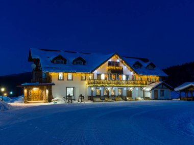 Gornaya Salanga kayak merkezinde Alp tarzı bir otel. Gece başlıyor, içinde samimi bir ışık yanıyor.
