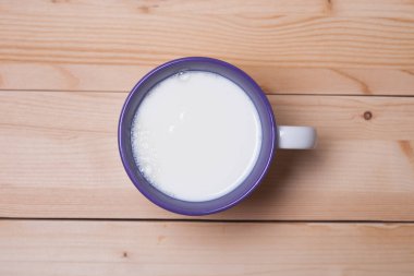 Ahşap bir yüzeyde sütlü kupa. Yukarıdan bak. Mor kupada beyaz süt