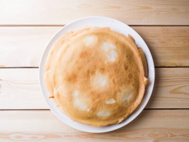 Krepler tahta bir yüzeyde, beyaz yuvarlak bir tabakta yatarlar. Yukarıdan görüntüle