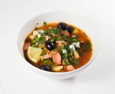 Beyaz bir tabakta Rus Solyanka çorbası. Hafif bir arkaplanda