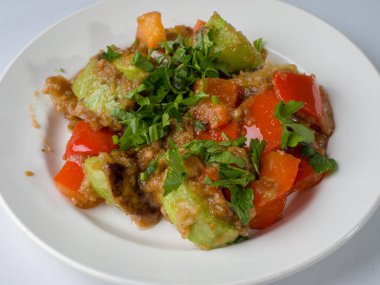 Yuvarlak beyaz tabakta kabak ve biberli sıcak salata. Yakın plan.