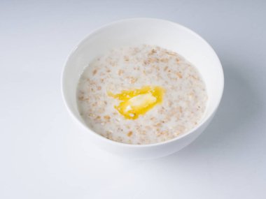 Süt içinde yulaf ezmesi, arka planda beyaz yuvarlak bir kasede tereyağı. Yan görünüm