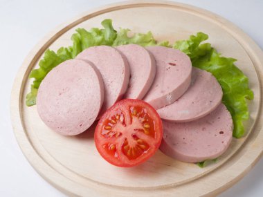 Kaynamış sosis, tahtanın üzerinde dilimler halinde kesilmiş. Marul yaprağı ve domatesin yanında