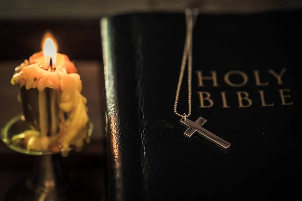 Cross on Bible with candle on an old oak wooden table. — Stock Photo, Image