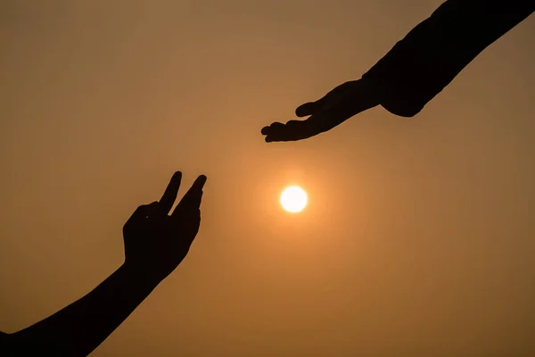 Giving a helping hand on the background of the sunset. Silhouette of helping hand concept and international day of peace.