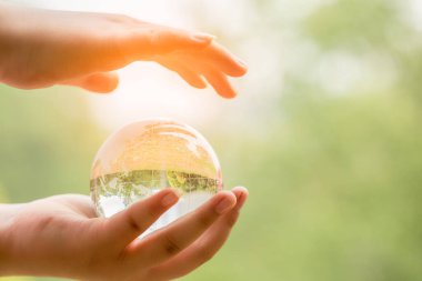 Dünya Günü için kart. Bulanık yeşil arka planda mavi gezegen kristal cam küresi insan elinde. Çevre tasarrufu, temiz gezegen ve ekoloji, sürdürülebilir yaşam tarzı kavramı.