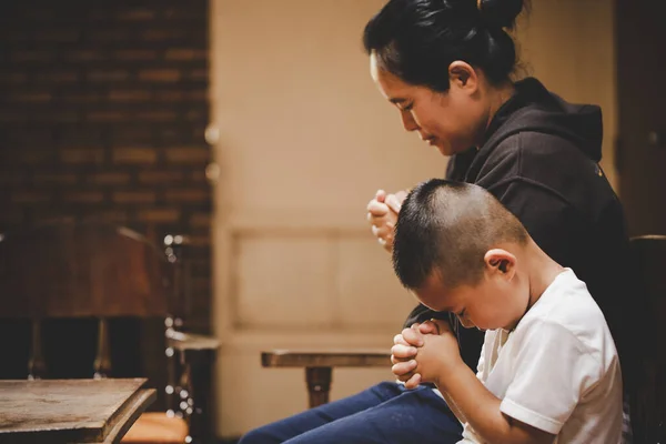Mother and son praying and praising God at home, sitting on wooden sofa  in living room