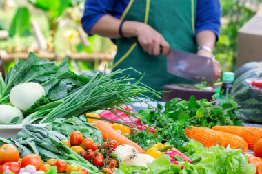 Çeşit çeşit olgun meyve ve sebzeler ve bulanık bir aşçı sebzeleri keser..