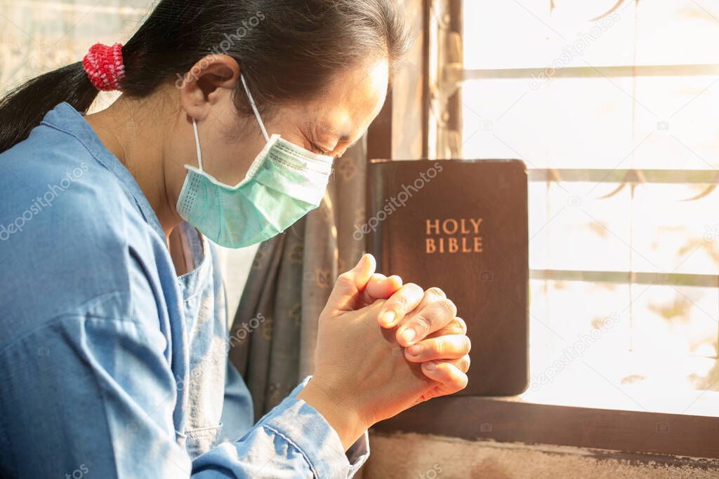 Asian woman wearing medical mask and praying for whole people in the world which got infected by novel Coronavirus, Covid-19 to get recovered soon.
