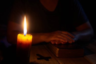 Dua eden kadın, karanlık bir kilisede dini mumlar, din ve inanç kavramlarıyla parlayan bir ibadet sırasında eski kutsal kitaba el uzatıyor.