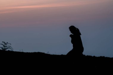 Kadın silueti dağda diz çöküyor ve güzel gündoğumu arka planında dua ediyor.