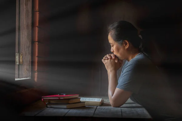 Woman praying in the morning. Asian girl hand praying on holy bible in wooden table, Hands folded in prayer concept for faith, spirituality and religion.