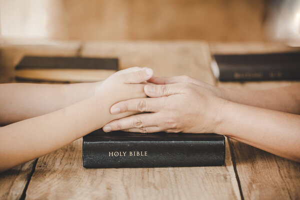 Couple mother and son are holding hands and pray together on wooden table with the light from side with copy space for your text