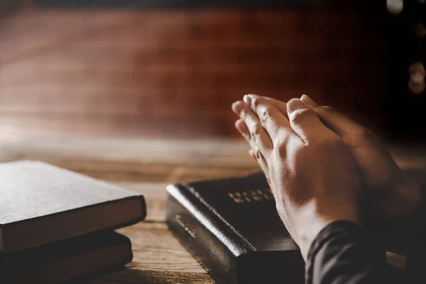 Praying hands of man on old bible over wooden table background