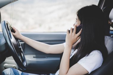 Kadın araba kullanırken telefonla konuşuyor.