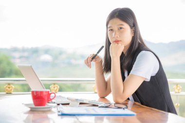 Güzel genç bir kadın, çatı katında oturmuş kahve içerken dizüstü bilgisayarda çalışıyor.