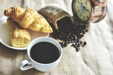 Kahve molası zamanı. Sıcak siyah amerikan kahvesi ve kruvasan pastanesi ve çuval bezinin üstünde ferahlatıcı bir öğleden sonra. Dünya Gıda ve İçecek Konsepti.