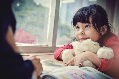 Şehir manzarasına karşı geniş pencereli annesiyle masal ödevi yapan ve öğrenen güzel bir kız. Ses tonunu süreç gibi ayır.