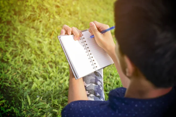 一个年轻英俊的小伙子在树下写日记 在湖畔花园的背景下 — 图库照片