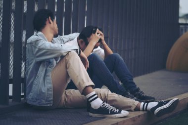 Üzgün Depresyon İki Uykusuzluk Adamı. İşini kaybettikten sonra kaldırımda oturuyorsun. Depresyonda olan genç bir adam yer altında oturuyor yüksek çelik kafes çitlerine yaslanıyor..