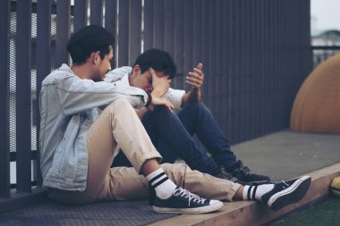 Üzgün Depresyon İki Uykusuzluk Adamı. İşini kaybettikten sonra kaldırımda oturuyorsun. Depresyonda olan genç bir adam yer altında oturuyor yüksek çelik kafes çitlerine yaslanıyor..