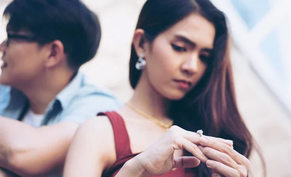 Closeup Sad Wife want to Divorce Lamenting Holding the Wedding Ring with Blurred Man selfie on travel outdoor. Upset young woman pulling wedding ring from finger. Ending bad relationships concept.
