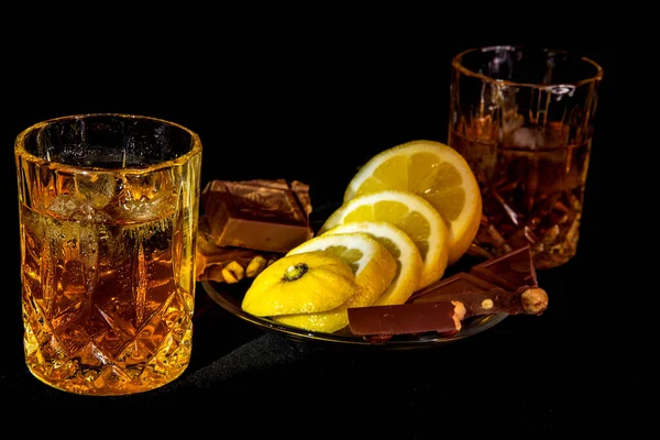 Dos vasos con una bebida y platillo de limón y chocolate sobre un fondo negro — Foto de Stock