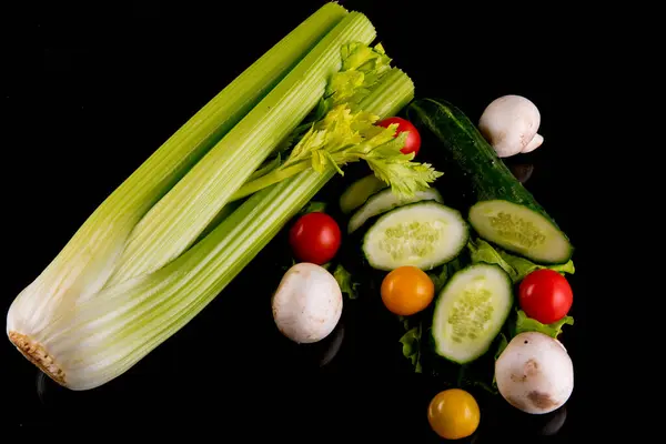 Celery, tomatoes, mushrooms, cucumbers, lettuce, cherry tomatoes, vegetable still life on a black background