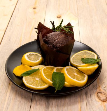 Siyah beyaz tabakta limon ve limon dilimleri, kek ve ahşap arka plan