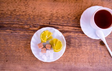 Bir kupa çay, limonlu tabak, sahora, ahşap arka planda.