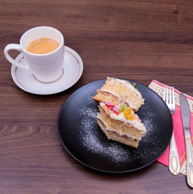 Siyah tabakta kek, bir kupa kahve, masada çatal bıçak.