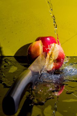  Damlalı kırmızı elmalar, sıçramalar, elma dilimleri, su, bıçak sarı arka planda.