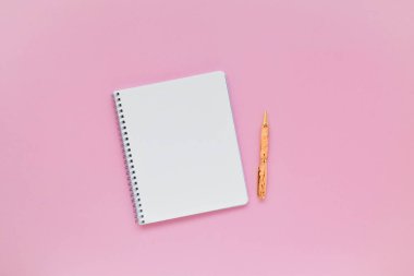 Pembe arka planda defter ve kalem, masada spiral defter. Flatlay, üst görünüm.