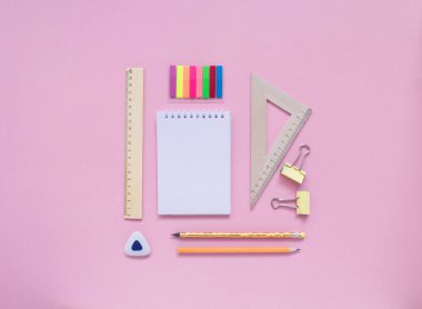 Sabit, okula dönüş, yaratıcılık ve eğitim konsepti. Not defteri, kalem, silgi, cetvel, ataç, zımba ve pembe arka planda fırça, düz yatak. Üst görünüm