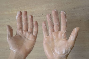 Beyaz tenli genç bej arka planda ellerini yıkıyor, sabunlu eller