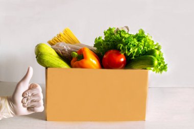 Yemek servisi. Yemek bağışı masada. Muhtelif konserve yiyecekler, tahıllar, makarna ve sebzeler ile karton kutuya yardım et. Gönüllü kutusu. Hijyenik eldivenli kadın eli.