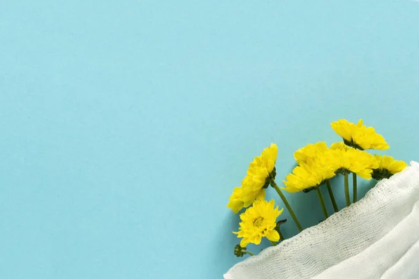 Seasonal spring summer allergy flowers concept. Yellow flowers with medical protective mask on blue background. Creative flat lay composition, copy space, minimal style