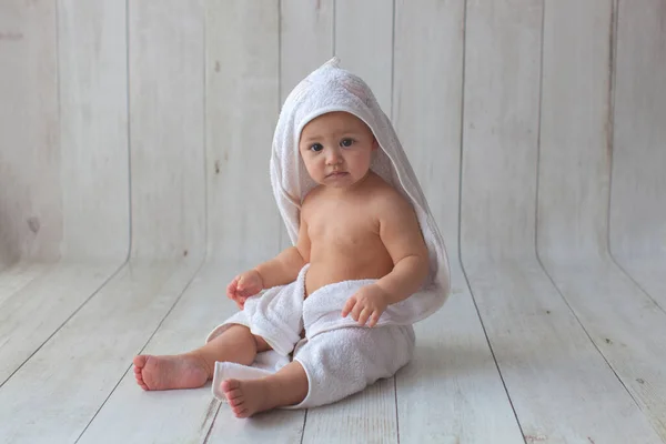 Piccolo bambino seduto in un asciugamano bianco su sfondo di legno . — Foto Stock