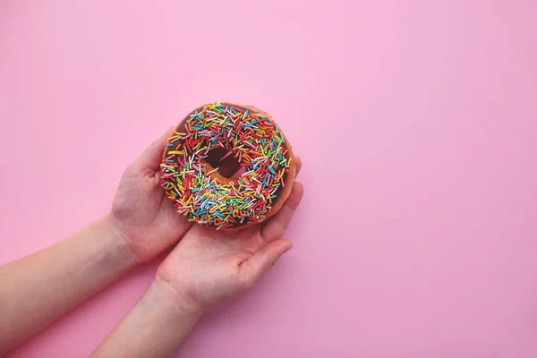 Donut de chocolate sobre fondo rosa en la mano . —  Fotos de Stock