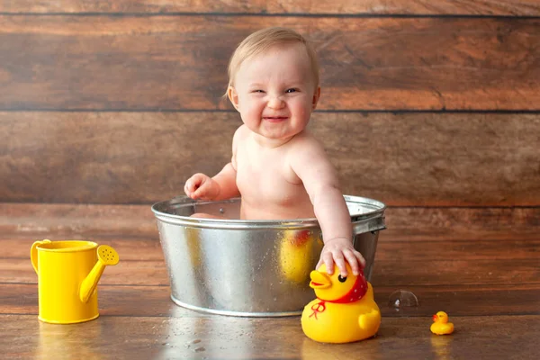 Kleines Baby nimmt ein Bad. Gummienten und eine gelbe Gießkanne. — Stockfoto