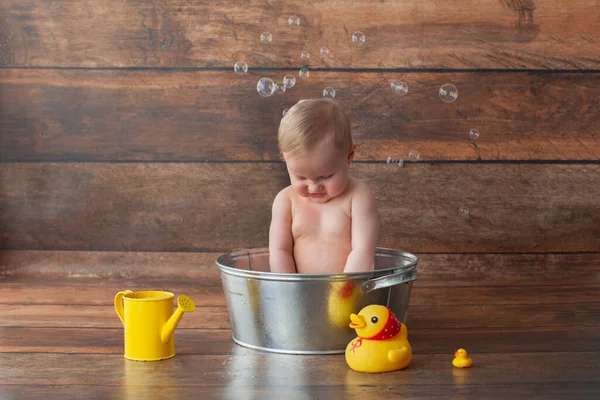 Kleines Baby nimmt ein Bad. Gummienten und eine gelbe Gießkanne. — Stockfoto