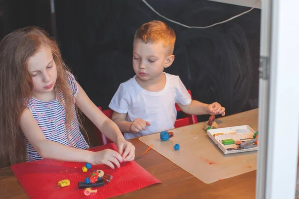 A girl of seven years and a boy of three years sit at the table and sculpt. — Stock Photo, Image