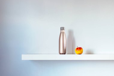 Su şişesi ve elma rafta, sağlıklı yaşam konsepti.