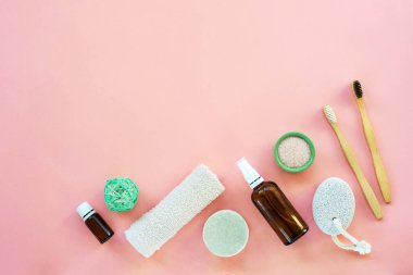 Hijyen ve vücut bakımı için düz aksesuarlar serildi: el yapımı sabun, sünger taşı, tahta diş fırçası, yüz toniği, pembe arka planda gerekli yağ ve pamuk havlusu. Üst görünüm, düz görünüm, kopyalama alanı.