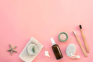 Hijyen ve vücut bakımı için düz aksesuarlar: el yapımı sabun, sünger taşı, tahta diş fırçası, yüz toniği, Himalaya tuzu ve pembe arka planda pamuk havlu. Üst görünüm, düz görünüm, kopyalama alanı.