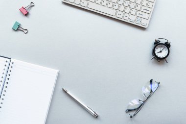 Dizüstü bilgisayarı, not defteri, çalar saati, gri arka planda kalemi ve gözlükleri olan bir çalışma masası. Ev kavramından çalış. Üst Manzara Düz Yat