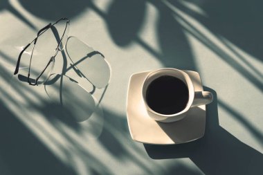 Güneş ışığında bir fincan kahve ve gözlük, üst manzara. Çalışma ya da öğrenim kavramı.