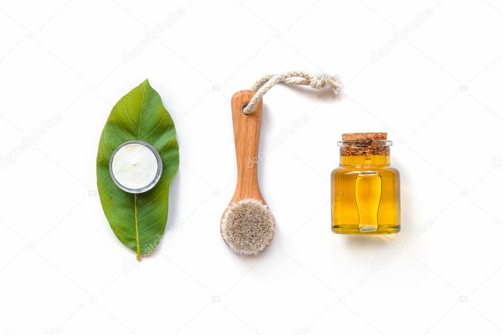 Wooden face brush, cosmetic oil and handmade cream. Eco-friendly spa, massage, peeling and hydration products. White background, top view, flat lay, copy space.