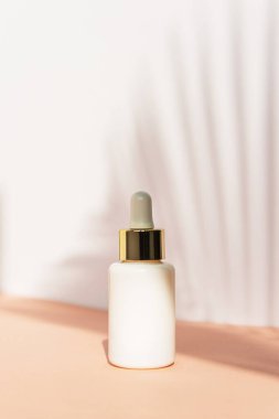 Kozmetik beyaz plastik şişe, arka plan olarak beyaz duvarda tropikal bitki gölgesi. Doğal cilt bakım ürünleri konsepti.