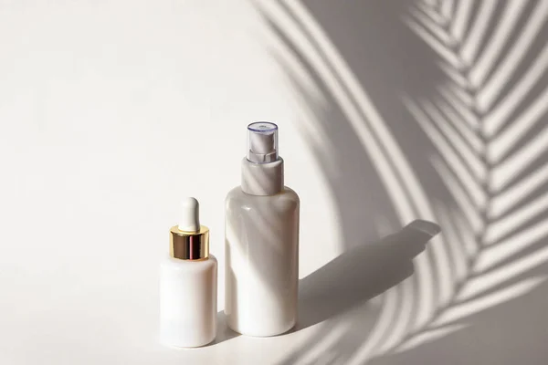 Cosmetische tonic en serum in blanco verpakkingen op een achtergrond van witte muur met palmbladeren schaduwen — Stockfoto
